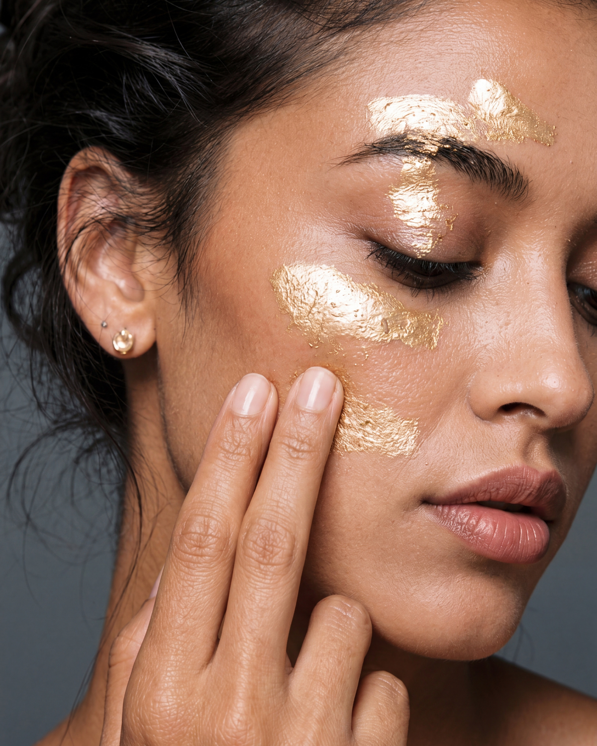 Woman with a gold face mask on her face against a gray background